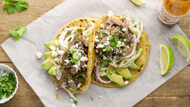 Two tequila-lime turkey tacos with avocado, slaw, cotija cheese, cilantro and lime wedges