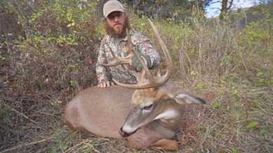 Hunter kneeling with a large whitetail buck, holding its antlers in brush