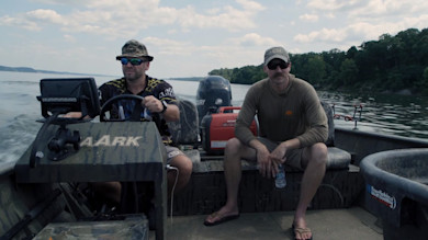 Two anglers in a motorboat on a river; console labeled AARK, fishfinder labeled HUMMINBIRD