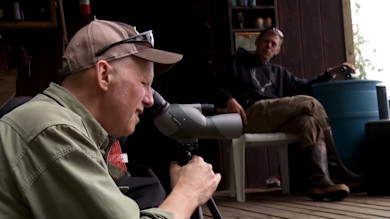 Man looking through Vortex spotting scope on tripod, another man seated on porch behind