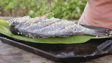 Whole steamed fish scored and sprinkled with minced garlic on a green leaf