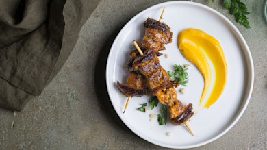 Turkey and date skewers with orange puree and parsley on a white plate