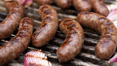 Grilled fresh sausages sizzling on a barbecue grate with charred red onion slices.