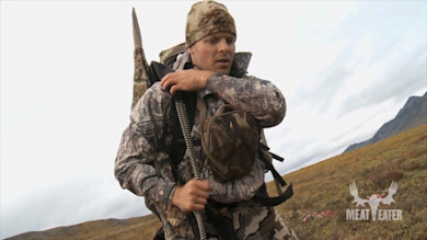 Hunter adjusting backpack straps on tundra, MEAT EATER logo overlay