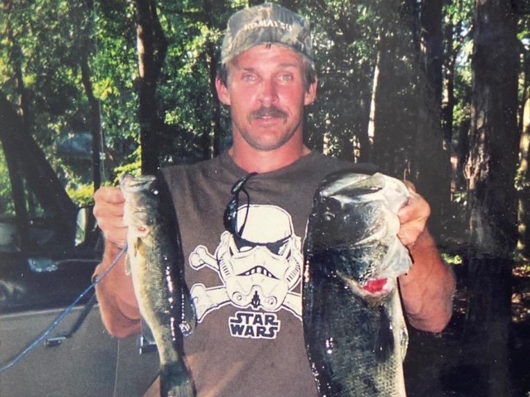 Man holding two largemouth bass, wearing t-shirt with Stormtrooper graphic and "STAR WARS"