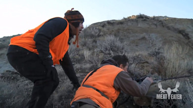 Two hunters in orange vests on hillside, one aiming rifle; visible text "MEAT EATER"
