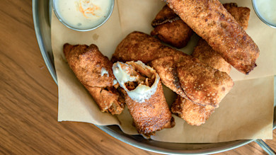 Fried turkey egg rolls on parchment-lined metal tray, one split open with dipping sauce