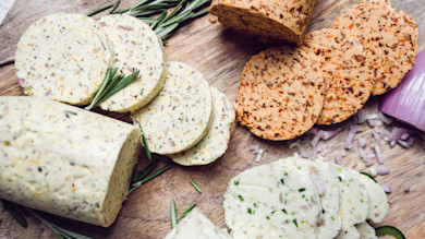 Sliced compound butters with rosemary sprigs and chopped shallot on a wooden board