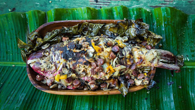 Whole roasted fish stuffed with sausage, mushrooms, and onions on banana leaves