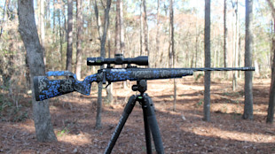 Bolt-action rifle with blue-and-black camo stock, scope and fluted barrel on tripod