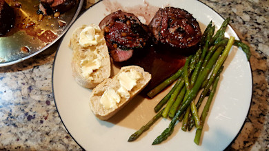 Rolled stuffed venison backstrap, pan sauce, sauteed asparagus and buttered baguette slices on plate