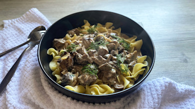 Bowl of beef and mushroom stroganoff over egg noodles with dill garnish