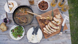 Sliced roasted turkey on cutting board stamped "MEAT EATER", pot stew, salad, pecans, bread