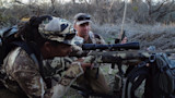 Two hunters aiming a camouflaged rifle in leafless brush