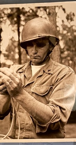 Man wearing military helmet and uniform ties rope in sepia-toned forest