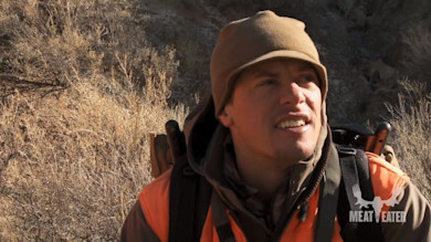 Steven Rinella wearing orange hunting vest and brown beanie; MEAT EATER logo