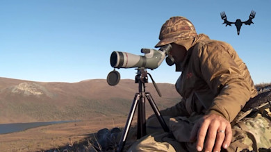 Man looking through spotting scope on tripod overlooking tundra, MeatEater logo at top right