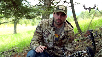 Hunter with compound bow kneeling under tree in camouflage jacket; MeatEater logo overlay