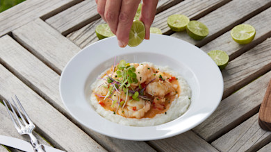 Hand squeezing lime over spiny lobster on coconut grits garnished with microgreens