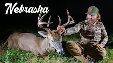 Nebraska: hunter seated beside large antlered buck holding antlers at night