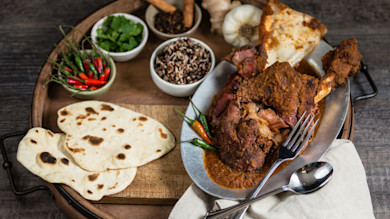 Venison vindaloo curry on metal platter with naan, wild rice, chilies, cilantro