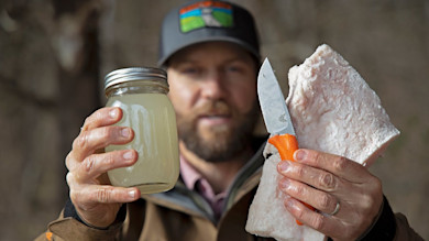 Man holding mason jar of rendered fat and a slab of fat with an orange-handled knife