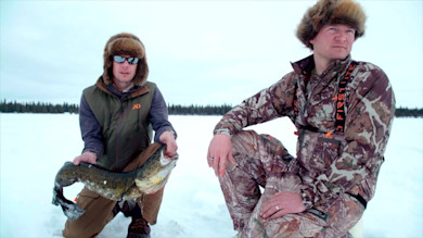 Two hunters on lake ice, one kneeling holding a burbot fish