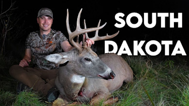 Hunter at night kneeling behind a large buck with antlers, blood on its nose; text "SOUTH DAKOTA"
