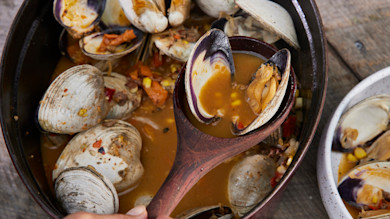 Steamed clams and smoked garlic sausage in broth with corn and peppers, wooden spoon