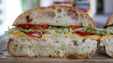 Ciabatta sandwich cut in half with tuna salad, cheddar, tomato, shredded lettuce