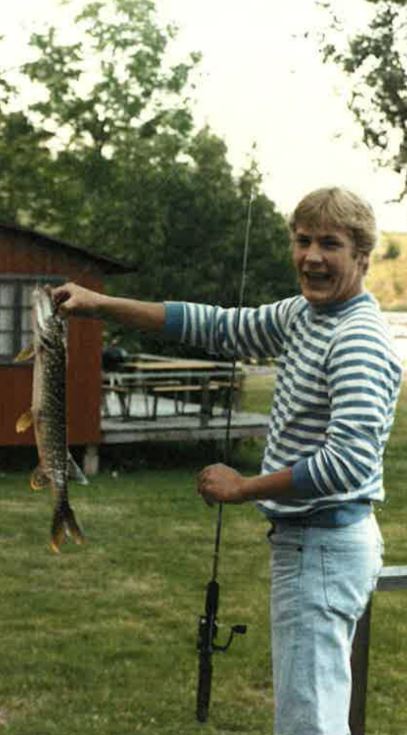 Young man smiling holding a large pike by the mouth with a fishing rod
