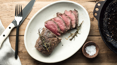 Reverse-seared venison steak sliced on white plate with rosemary and flaky salt