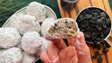 Powdered sugar-coated cookie bitten to show crumbly interior with dark flecks, hand holding