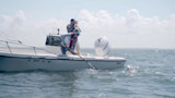Two anglers on skiff fighting a fish; woman gaffs near hull "DC 8910 AL" and outboard "HONDA"