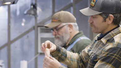 Preparing catfish fillets at a counter; man on right holds a fillet, other man blurred behind