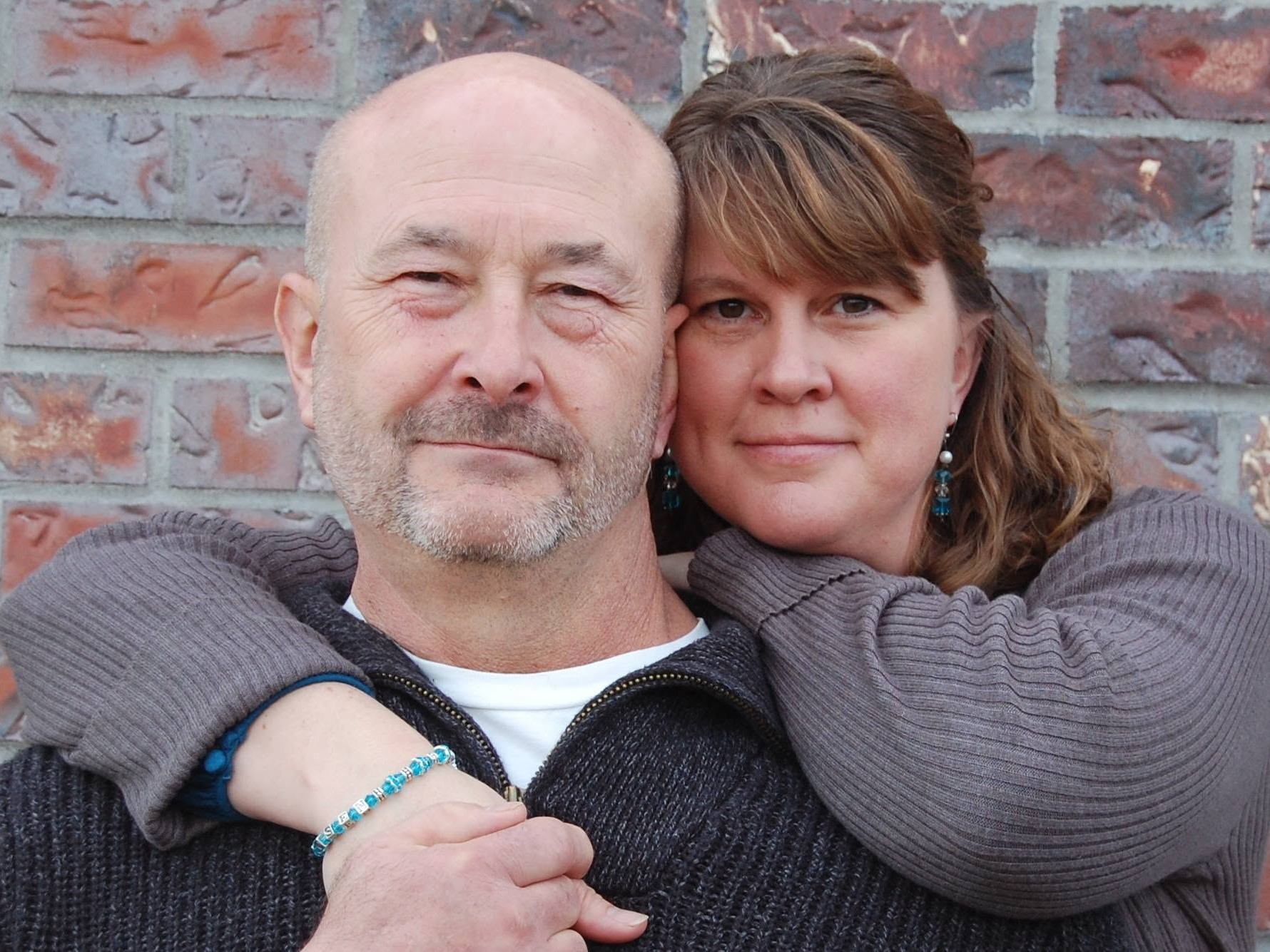 Man and woman embracing in front of a brick wall