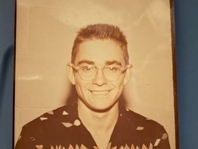 Smiling man wearing round glasses and patterned shirt, sepia-toned portrait on blue background