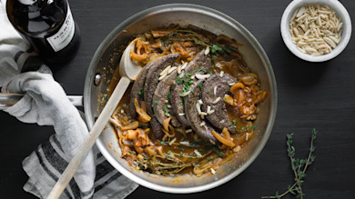 Sauteed sliced liver and caramelized onions in skillet, topped with slivered almonds and parsley
