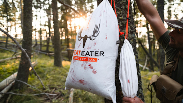 MeatEater grocery bag stained with blood hanging from a tree; man holding orange rope