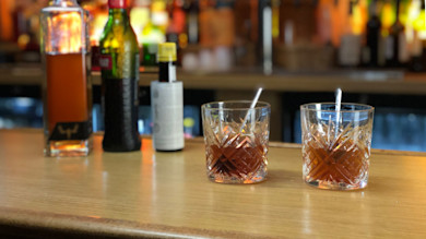 Two old fashioned cocktails in cut crystal glasses with metal stirrers on a wooden bar