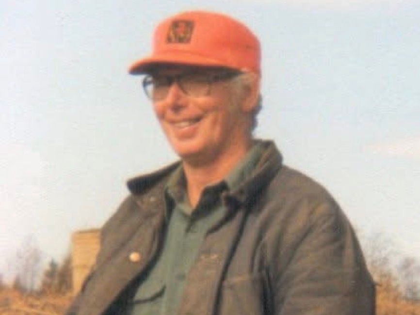 Smiling man in orange cap and glasses wearing a jacket outdoors