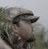 Man in camouflage jacket and cap with hood up, side profile