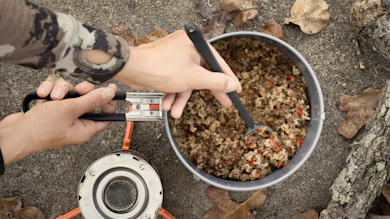 Hands stirring dehydrated venison taco bowl in camping pot over backpacking stove