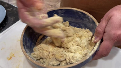 Two hands breading oysters in seasoned flour in a blue mixing bowl