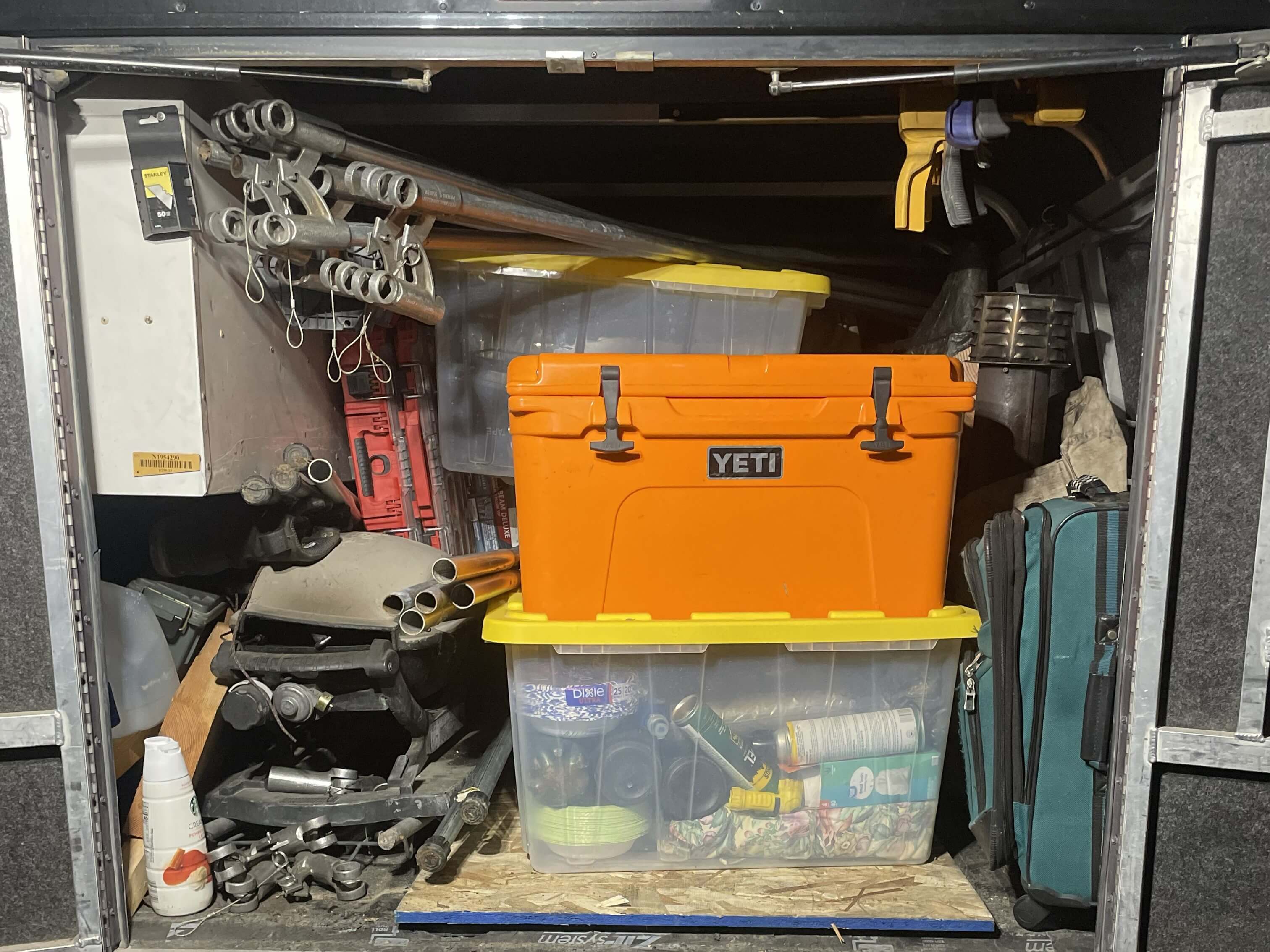 Orange YETI cooler in packed trailer storage with clear bins, metal poles and tools