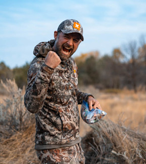 Hunter in camouflage pumping fist, holding a plastic snack bag in dry field