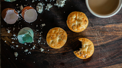 Three venison-and-egg mini muffins on a wooden board with broken eggshells and coffee