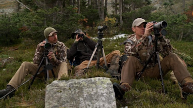 Three hunters seated on an alpine slope using spotting scopes on tripods