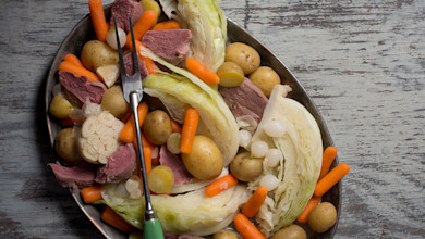 Corned goose breast with cabbage wedges, baby potatoes, carrots, pearl onions and garlic head on platter