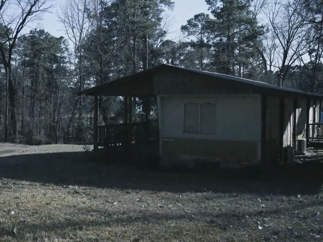 Small single-story house with covered porch and trees in the background